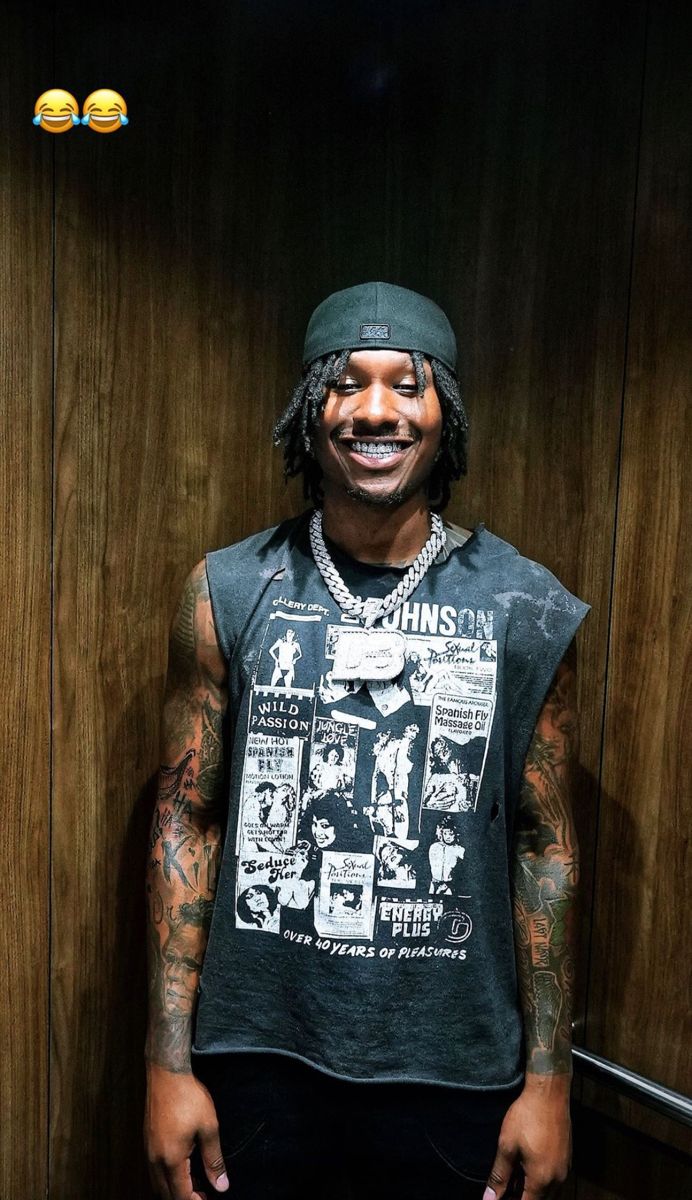 a man with tattoos standing in front of a wooden wall