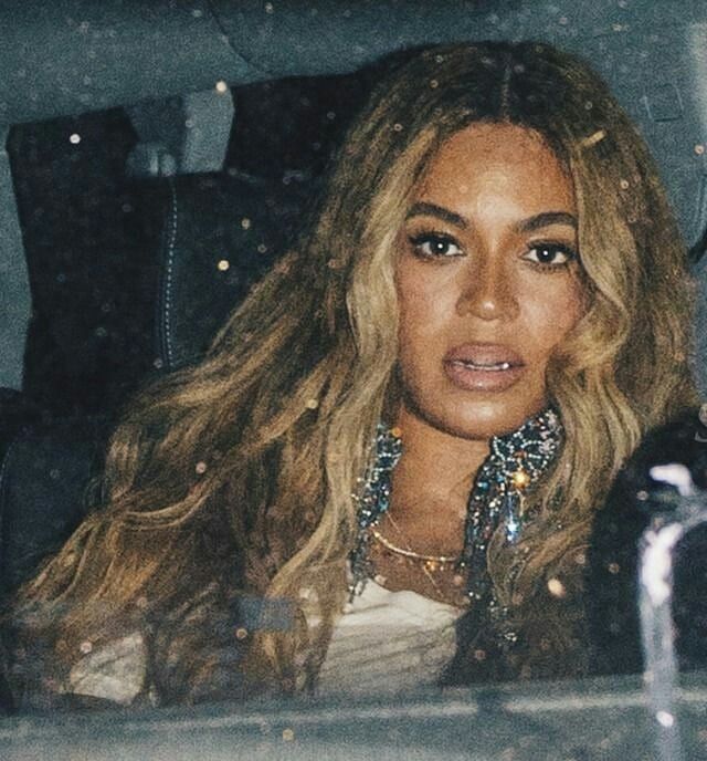 a woman sitting in the back seat of a car with long blonde hair and jewelry on her neck