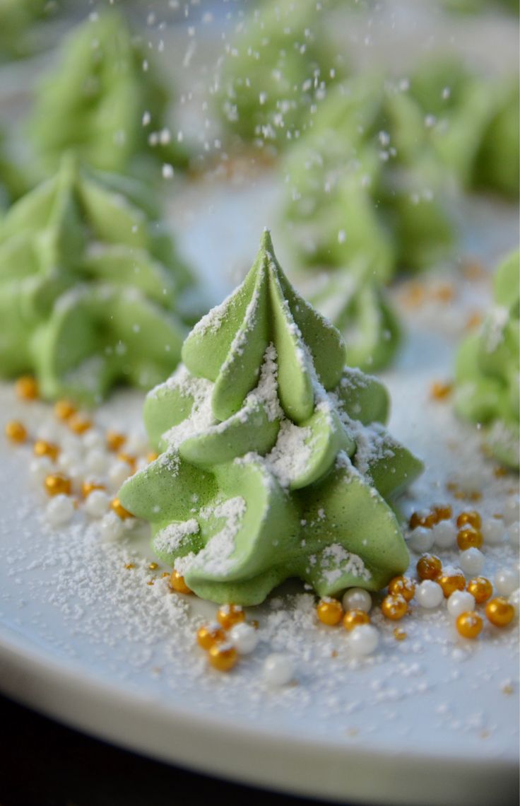 some green desserts on a white plate with sprinkles and powdered sugar