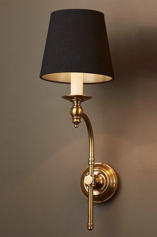 a wall light with a black shade on it's side and a white lamp in the corner