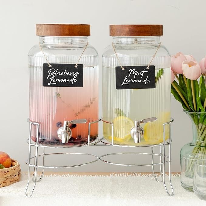 two glass jars with labels on them are sitting next to some flowers and fruit in vases