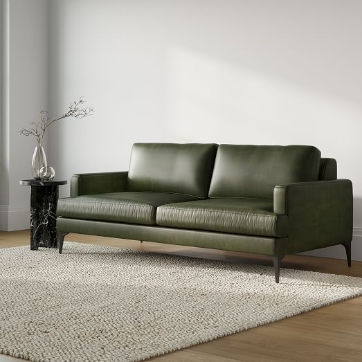 a green leather couch sitting on top of a wooden floor next to a white rug