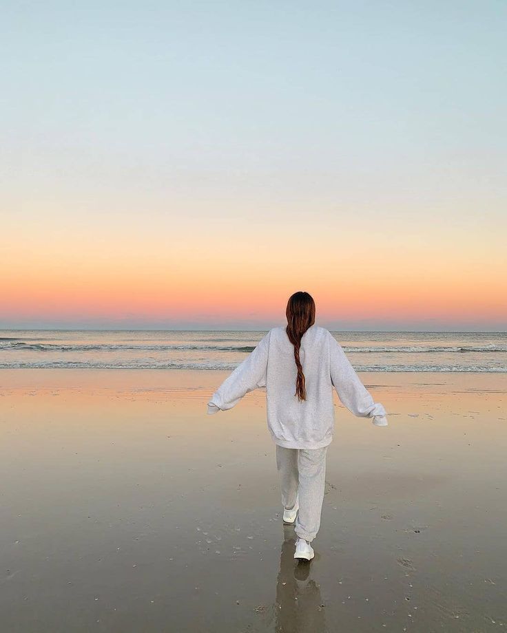 a woman walking on the beach at sunset