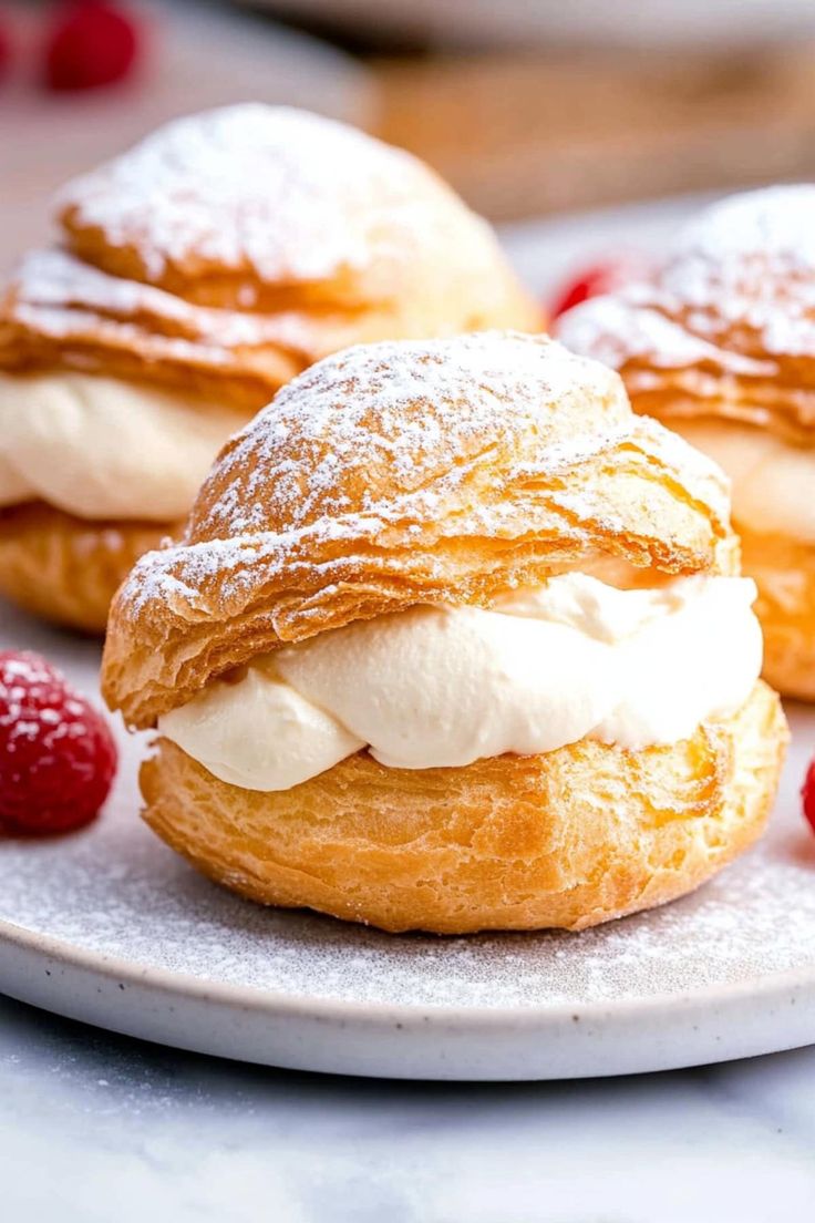 three pastries on a plate with raspberries and powdered sugar in the background