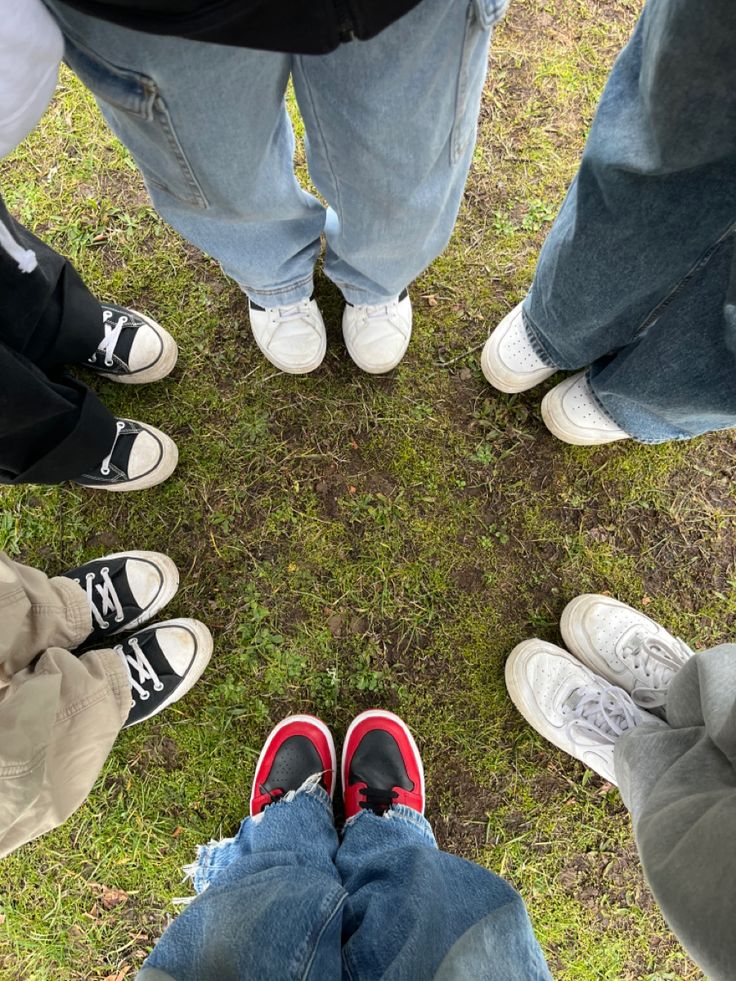 four people are standing in a circle on the grass with their feet up and one is wearing red shoes