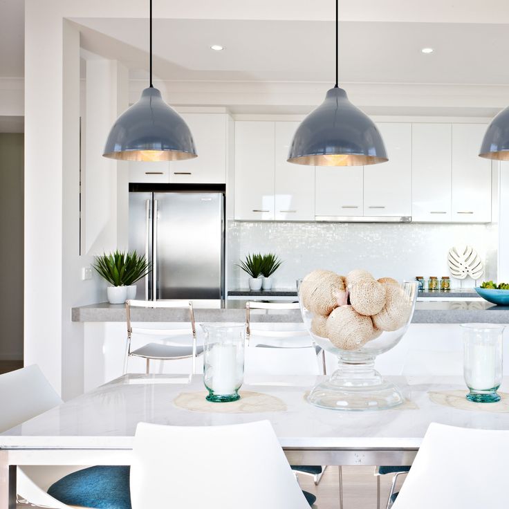 a white kitchen with blue accents and pendant lights hanging over the countertop, surrounded by chairs