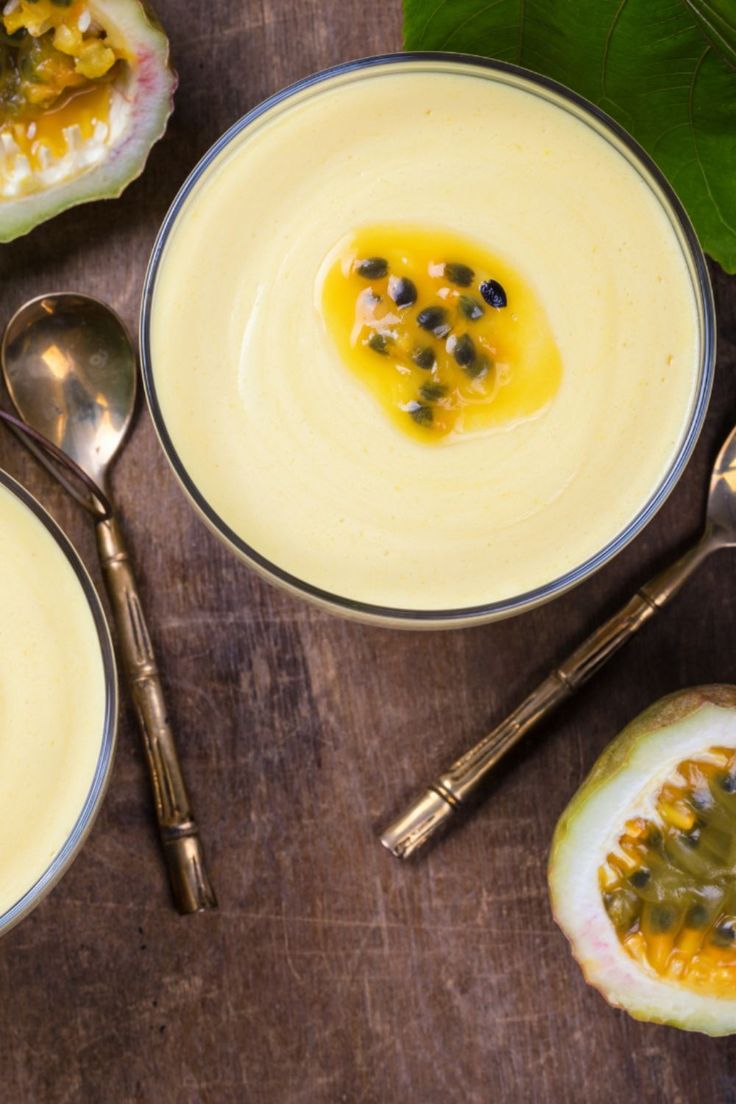 two bowls filled with food on top of a wooden table next to silver spoons