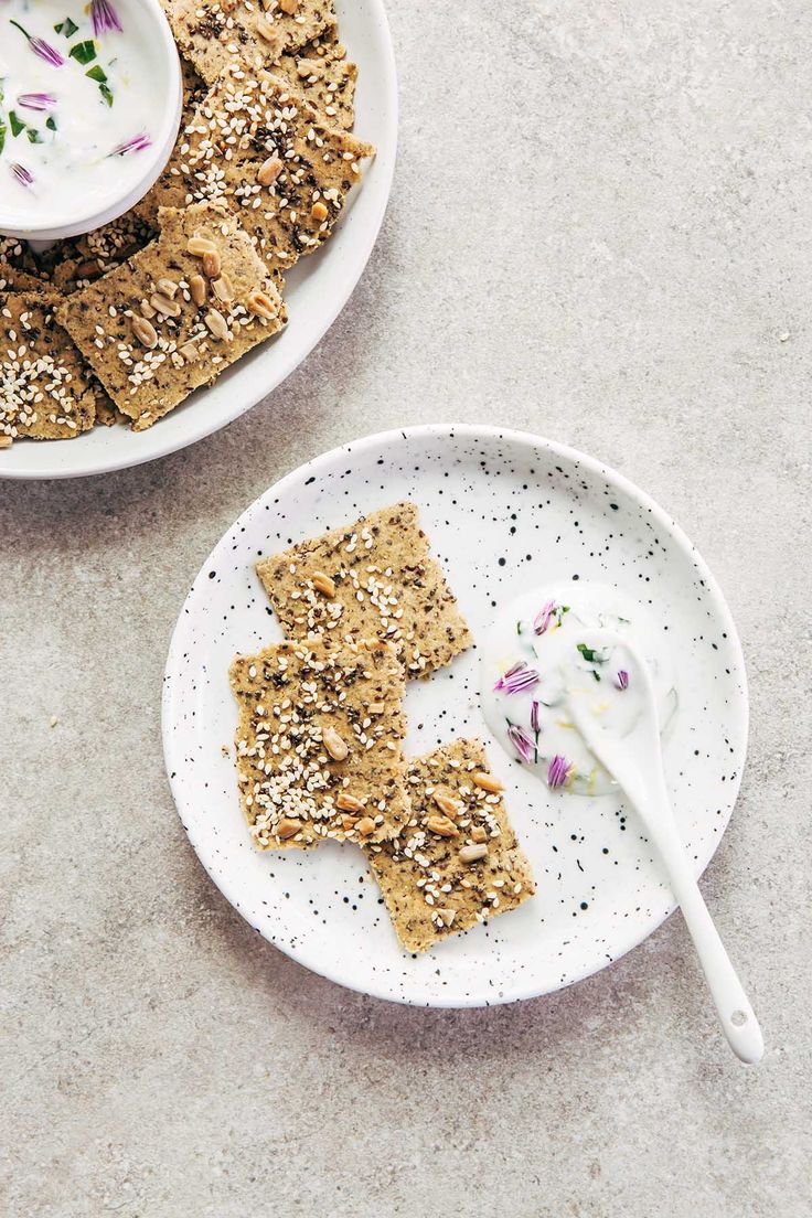 two white plates with crackers on them next to a bowl of yogurt