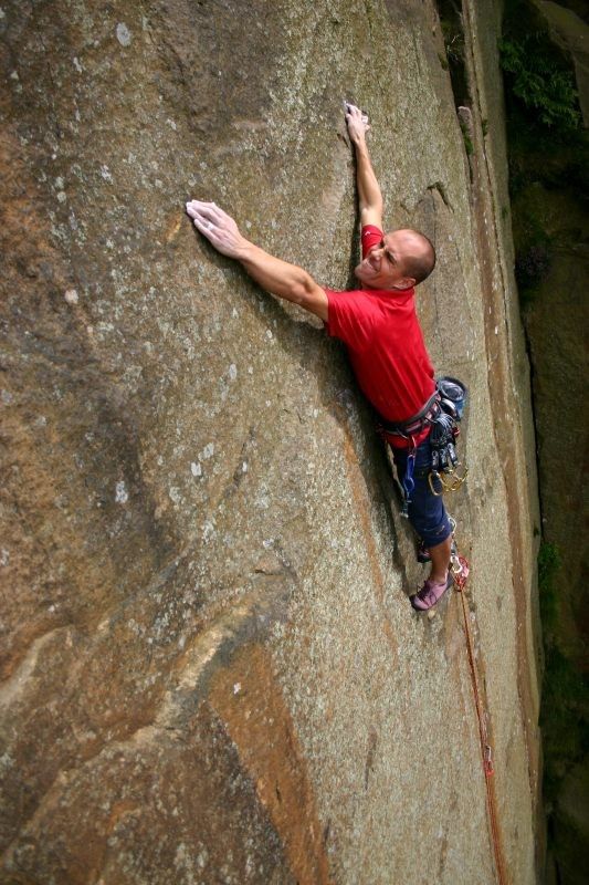 a man climbing up the side of a large rock with his hands in the air