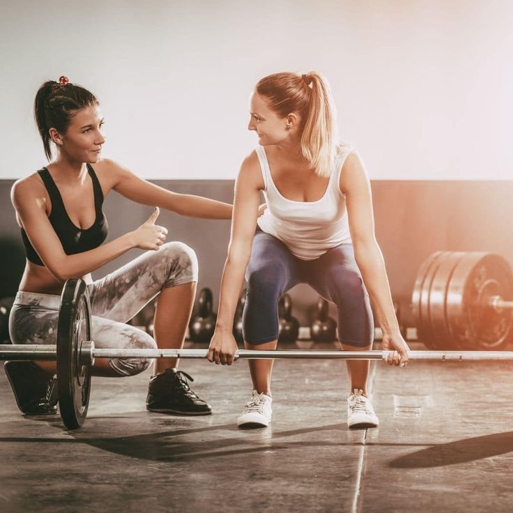 two women are squatting while holding barbells