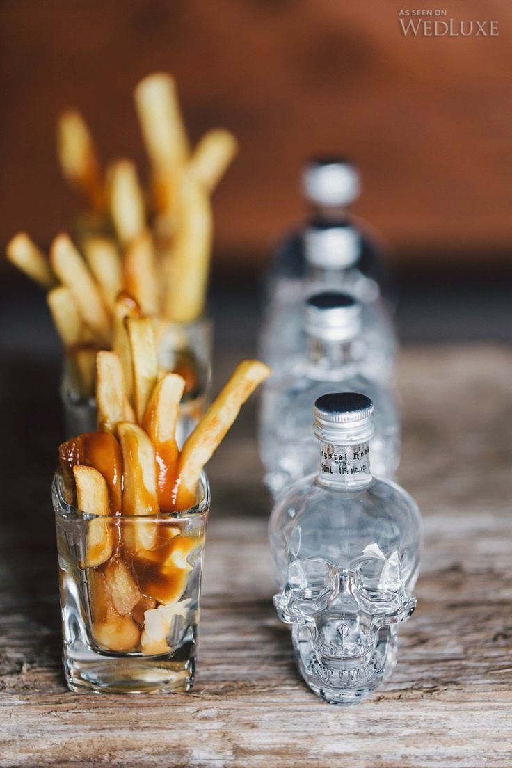 french fries are in a glass next to a bottle of water on a wooden table