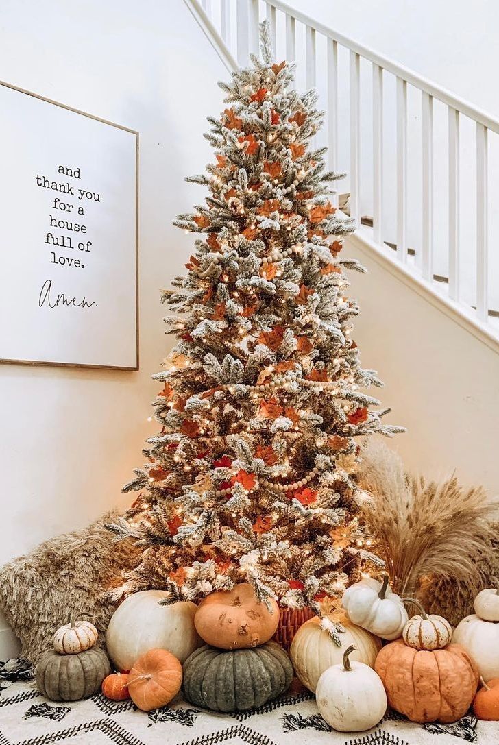 a decorated christmas tree sitting in front of a stair case with pumpkins and other decorations