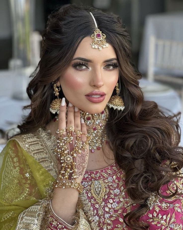 a woman in a bridal outfit with jewelry on her hand and hands near her face