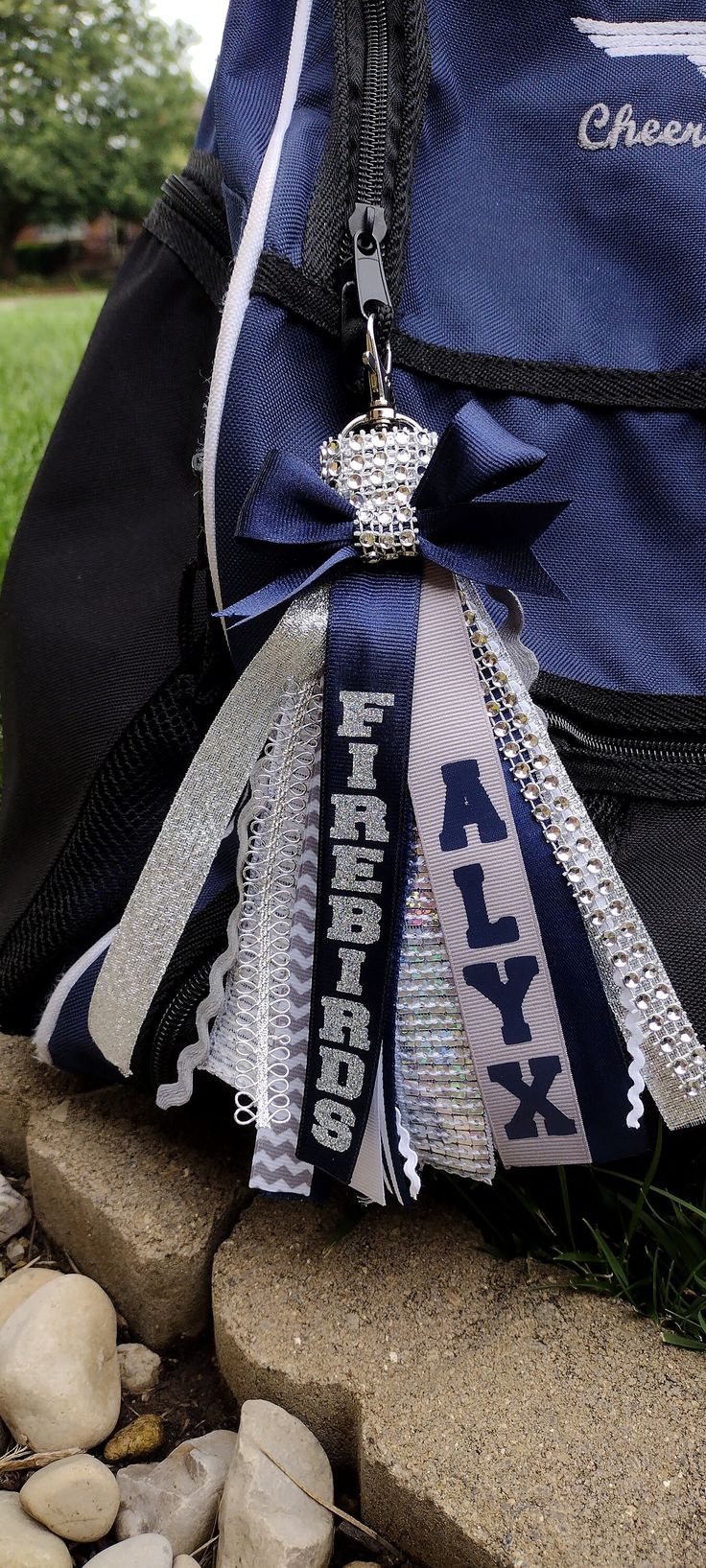 a blue and white backpack with silver ribbons on it's side sitting on some rocks