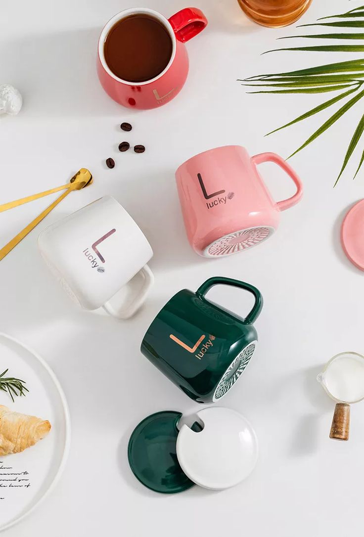 coffee mugs, tea cups and other items on a white surface with palm leaves