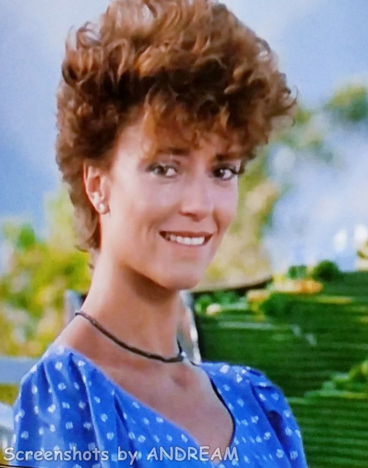 a woman with curly hair is smiling at the camera while wearing a blue dress and necklace