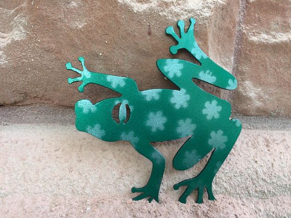 a green metal frog sitting on top of a stone wall next to a brick wall