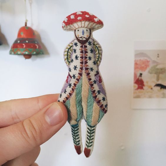 a person holding up a tiny doll with a mushroom hat on it's head