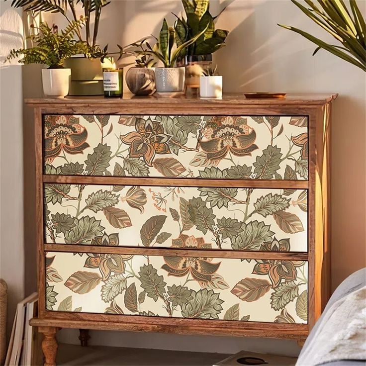 an old dresser with flowers and leaves painted on the drawers is sitting next to a plant