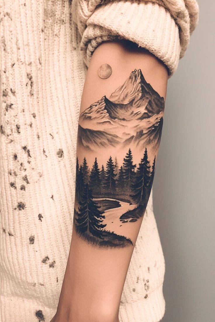 a woman's arm with a mountain scene and pine trees tattoo on the forearm