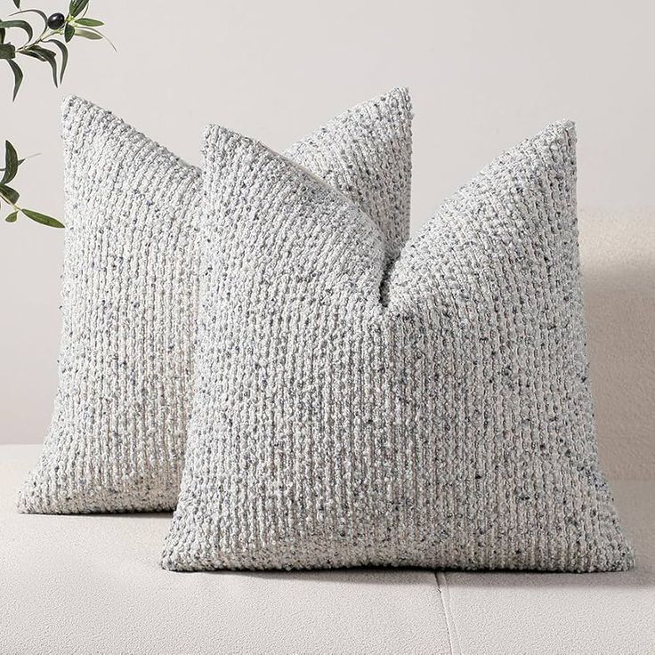 two gray pillows sitting on top of a white couch next to a potted plant