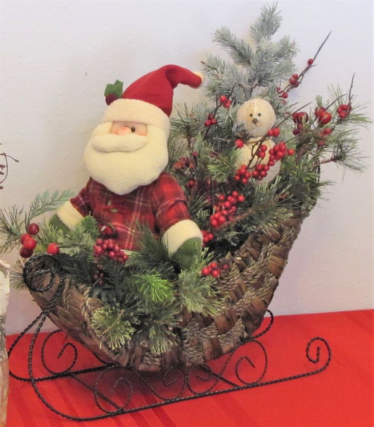 a stuffed santa clause sitting in a basket with pine branches and berries on the table