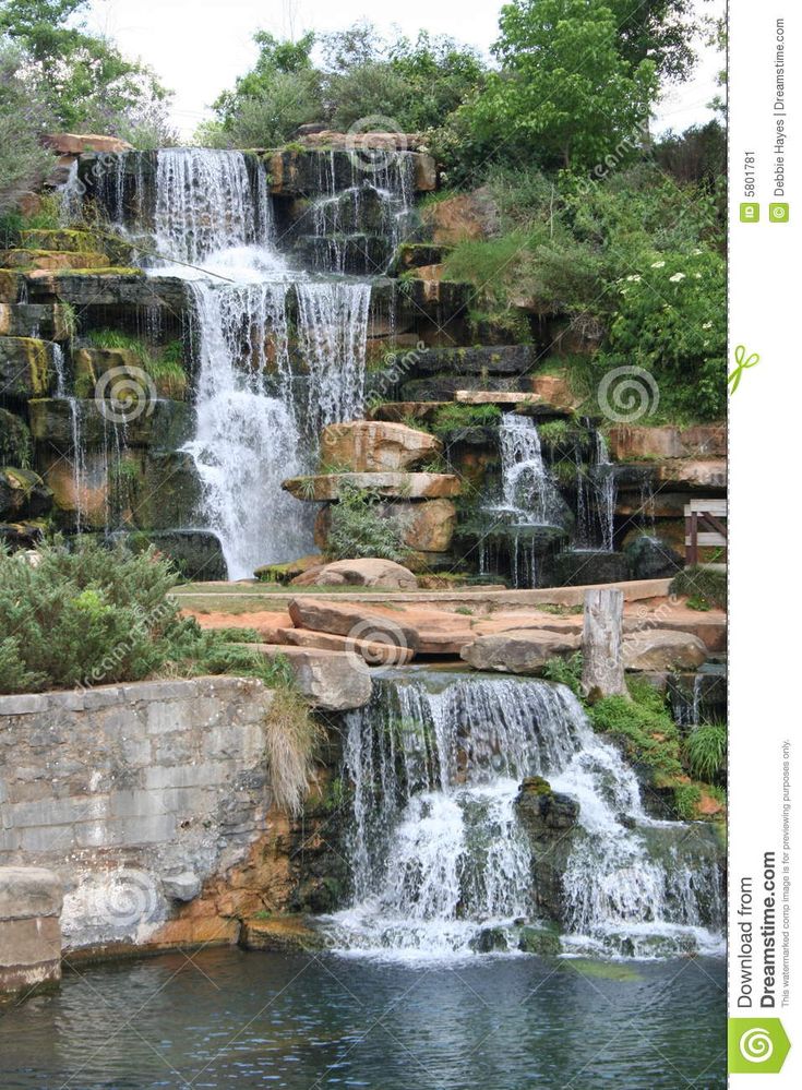 a large waterfall is in the middle of a pond with rocks and trees around it