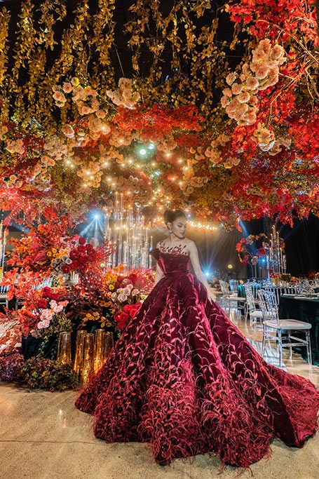 a woman in a red dress standing under a tree filled with flowers and lite up lights