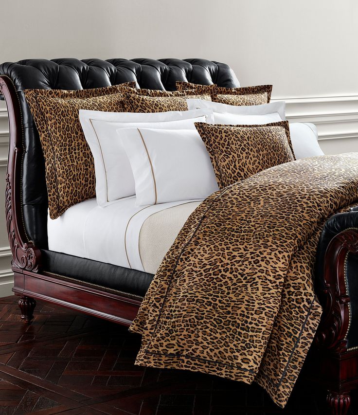 a leopard print comforter set on a bed with black leather headboard and foot board