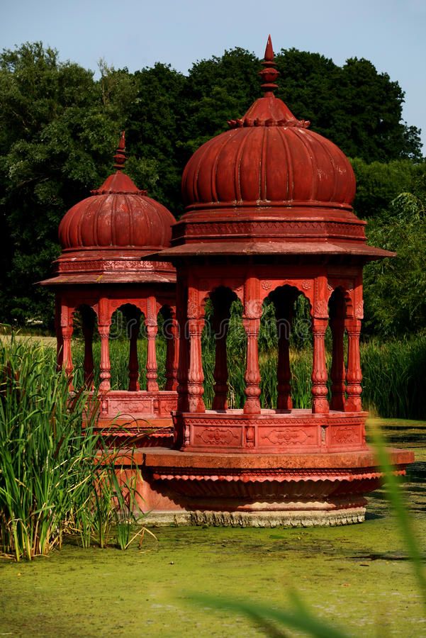 an old red gazebo in the middle of a pond