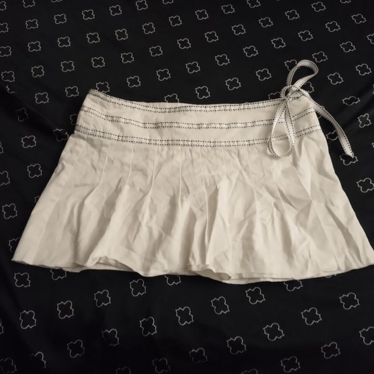 a white skirt is laying on top of a black and white bed spread with an attached tie