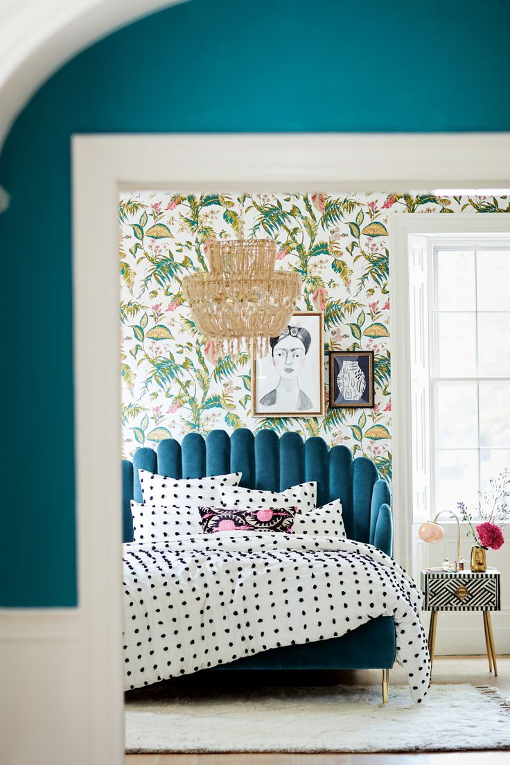 a bedroom with blue and white wallpaper has a bed in the corner, next to a window