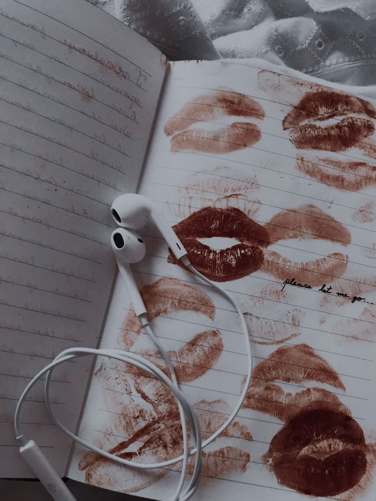 an open book with lipstick drawn on it next to headphones and earbuds