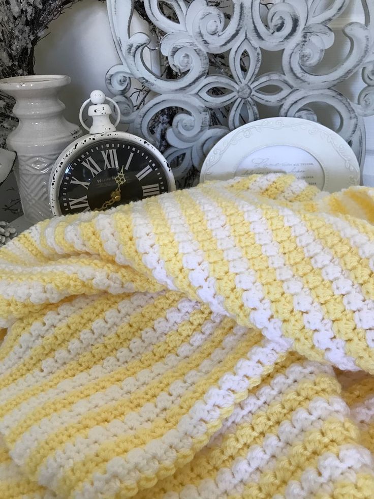 a yellow and white blanket sitting on top of a bed next to an alarm clock