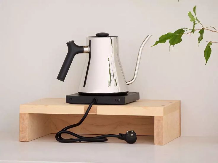 an electric tea kettle sitting on top of a wooden shelf next to a potted plant