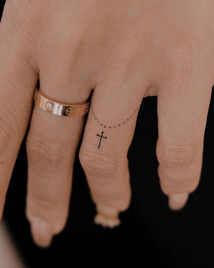 a woman's hand with a cross tattoo on the middle finger and small dots around it