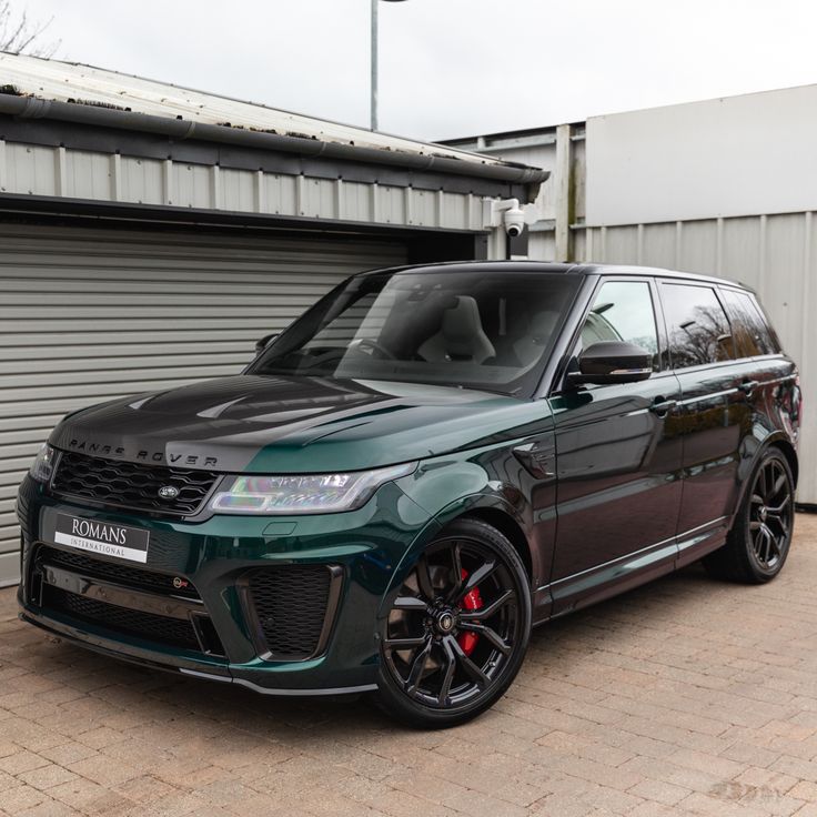 a green range rover parked in front of a garage