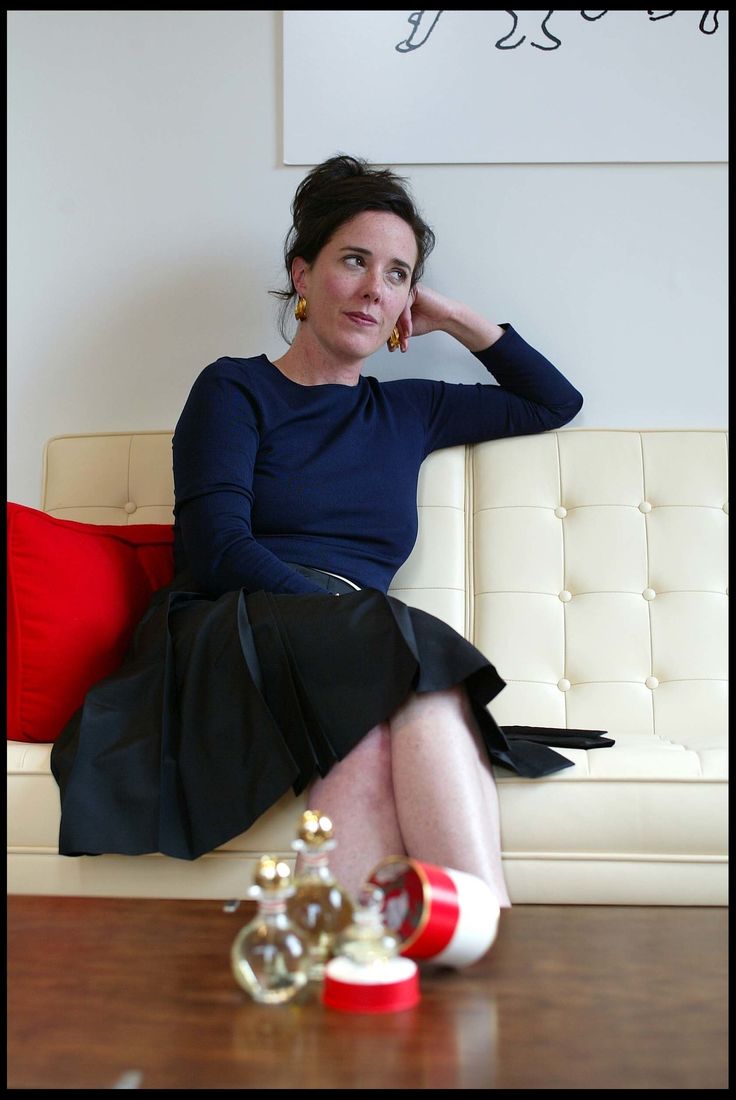 a woman sitting on top of a white couch next to a red and white pillow