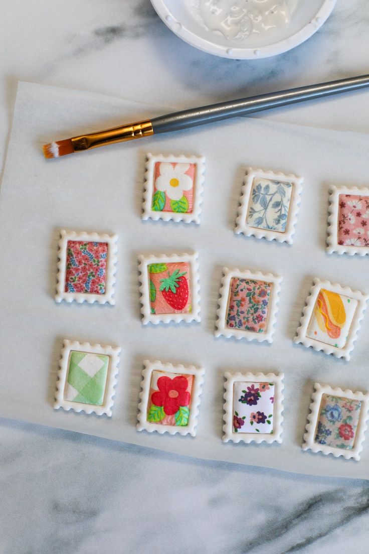 some stamps are sitting on a table next to a paintbrush and watercolor pencil