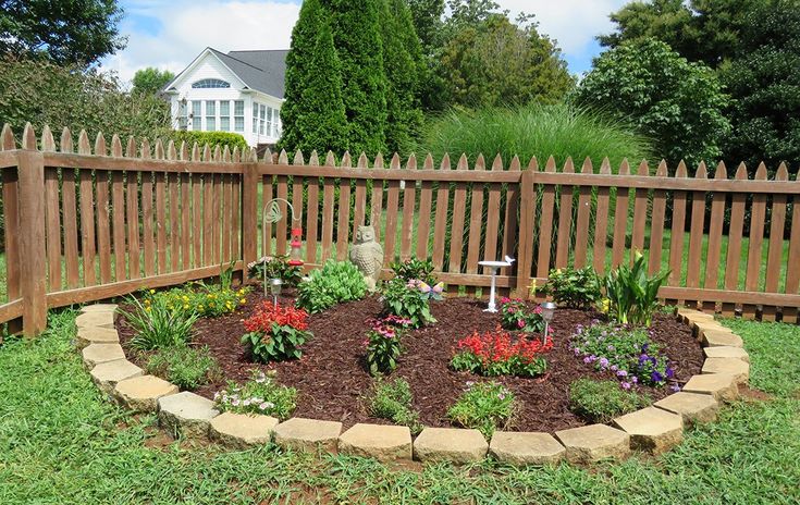 a flower bed in the middle of a yard next to a wooden fence and house