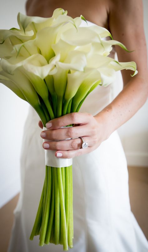 a woman in a wedding dress holding a bouquet of white calla lilies and green stems