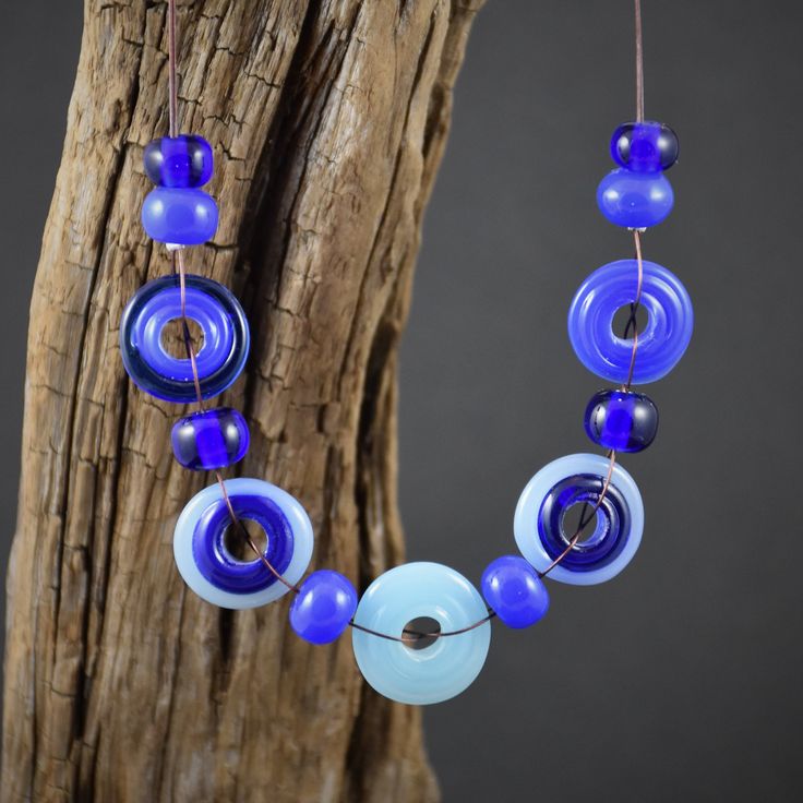 a blue and white beaded necklace hanging from a wooden tree branch on a gray background