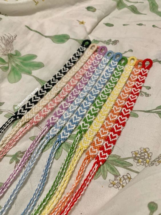 six different colored braided bracelets on a white fabric with flowers and leaves in the background