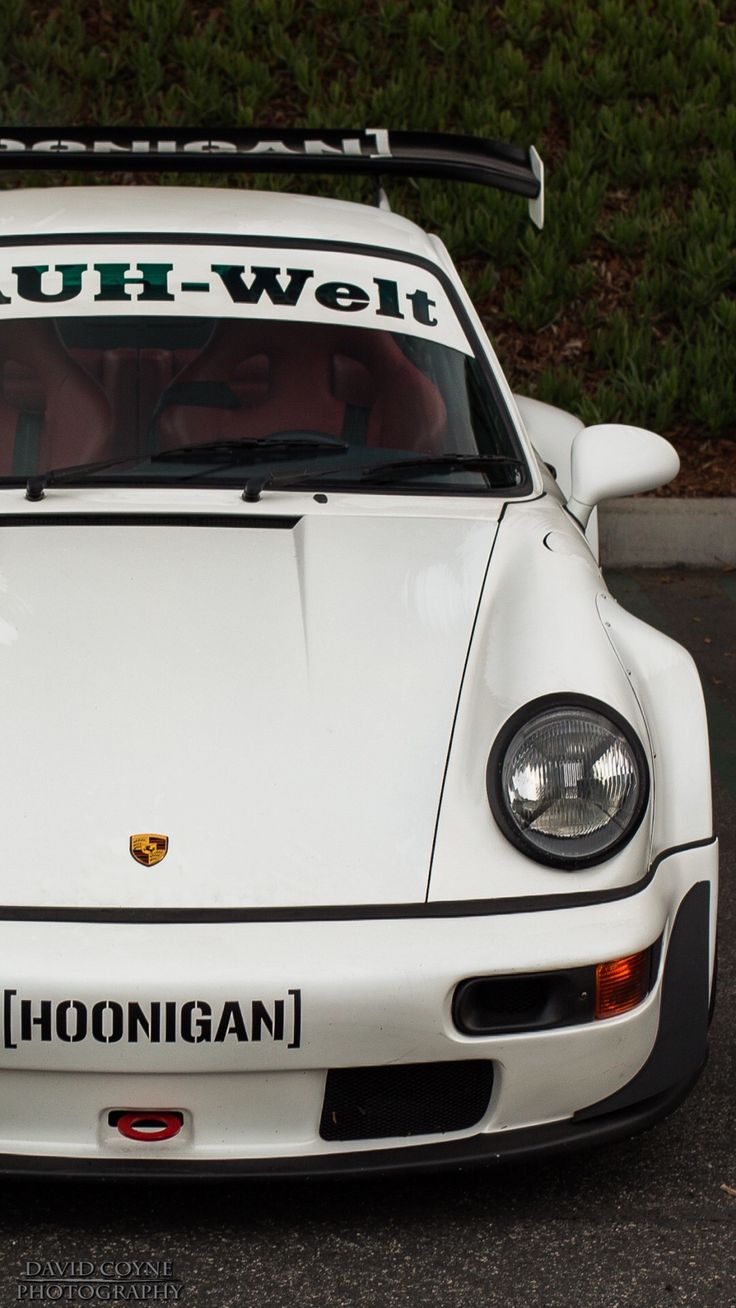 a white sports car parked in front of a bush - welt sign on it's windshield