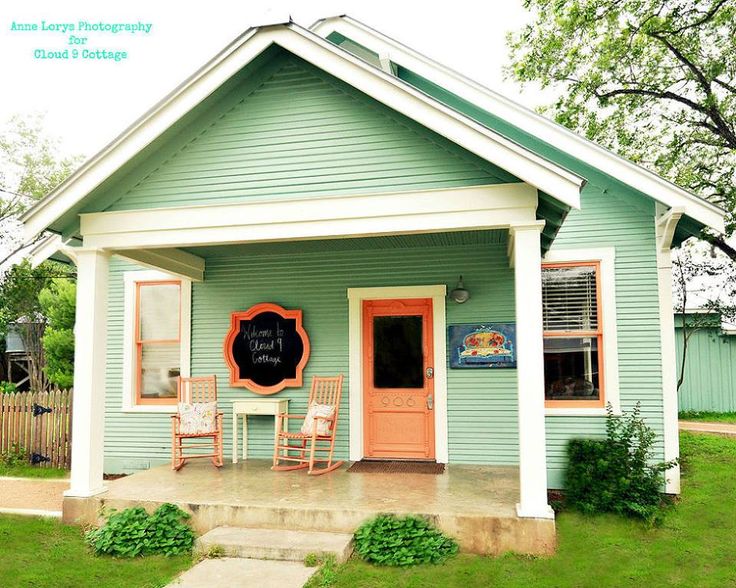 a small blue house with two chairs and a chalkboard sign on the front door