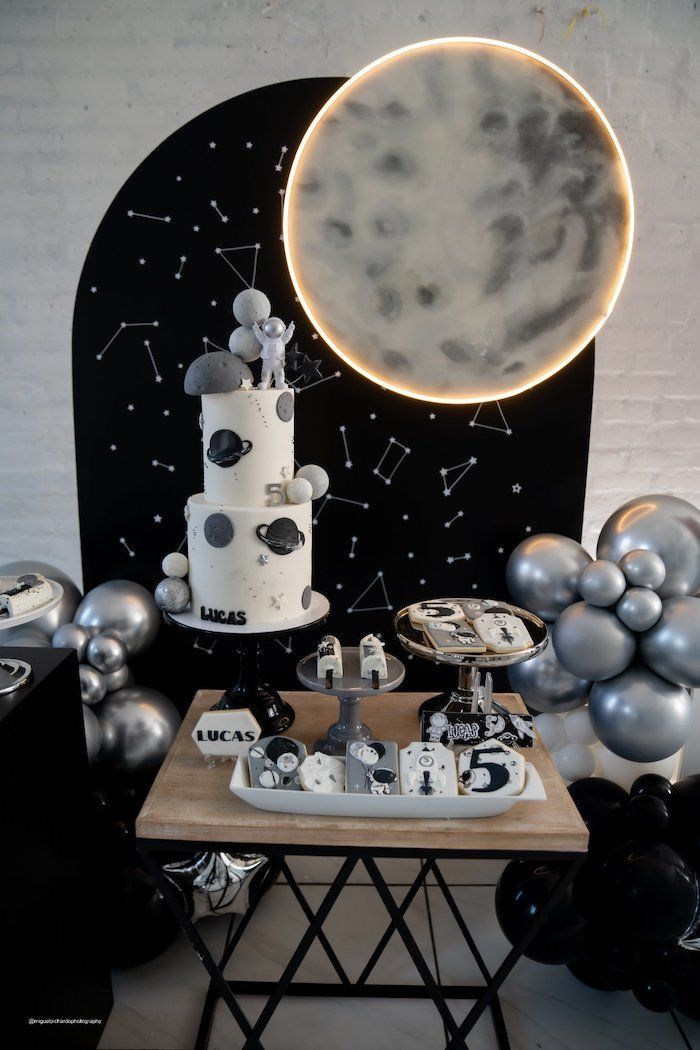 a table topped with a cake next to silver balloons and a moon on the wall