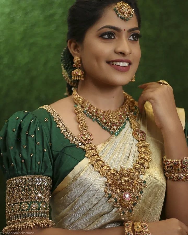 a woman in a green and white sari with gold jewelry on her neck, smiling