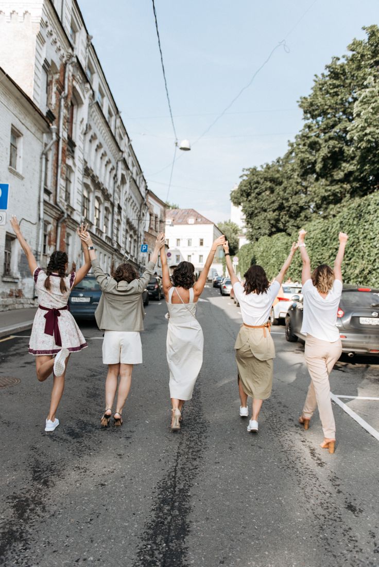 four women walking down the street with their arms in the air