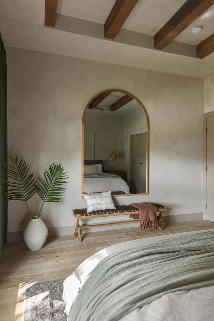 a bedroom with a bed, mirror and plant on the floor in front of it