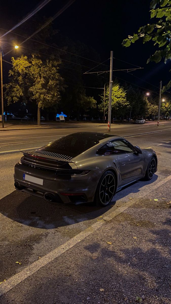 a grey sports car parked on the side of the road at night with its hood up